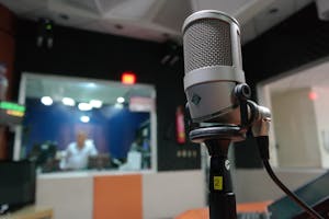 Close-up of a microphone in a recording studio with a blurred sound engineer in the background.